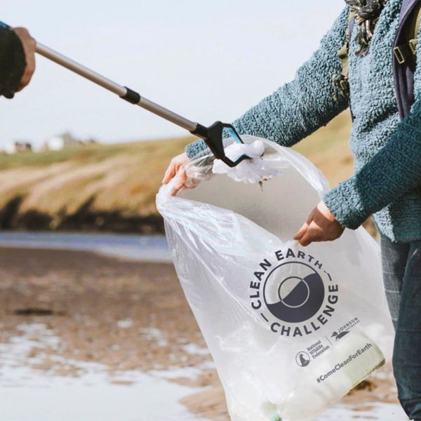 Two people pick up trash and put it in a bag on the beach
