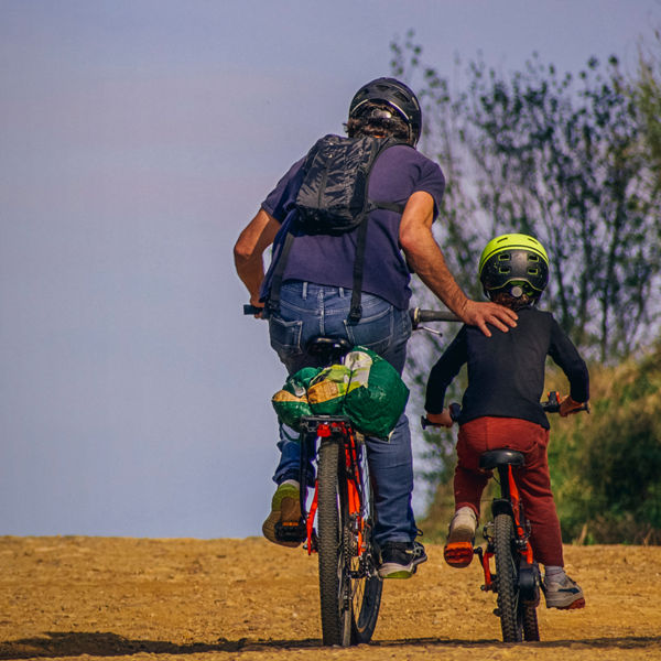 Father and son cycling up a hill. The father is helping his son by pushing him up the hill.