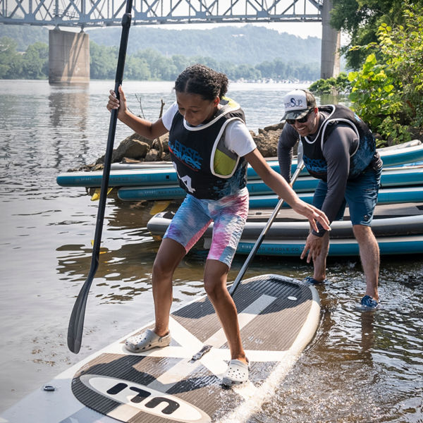 A girl stands up on a paddle board as part of First Waves