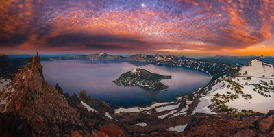 Man on hilltop viewing Crater Lake with a sunset at dusk