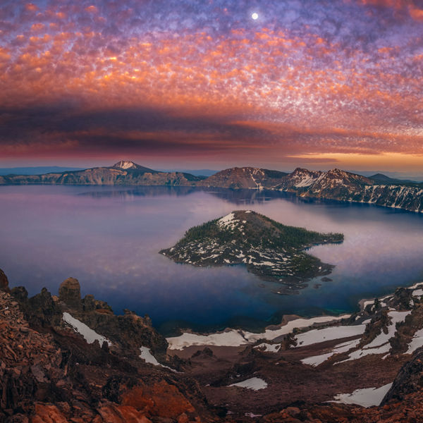 Man on hilltop viewing Crater Lake with a sunset at dusk