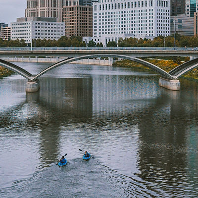 Two kayakers paddling in front of a bridge in Columbus