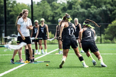 A group of girls huddled playing lacrosse. 