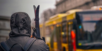A man holds skis in his hands waiting for public transport.