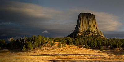 Golden light at sunset hitting Devil's Tower, aka, Bear Lodge, behind a hiking trail leading toward the pine forest at Devil's Tower National Monument, Wyoming