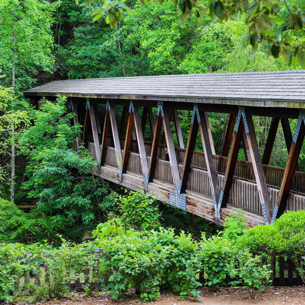 A long covered dark wood bridge over the Big Creek river surrounded by lush green lush green trees at Vickery Creek in Roswell Georgia