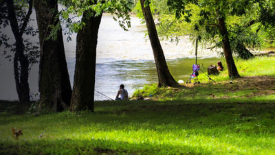 a man and a woman fishing along the Chattahoochee river surrounded by lush green grass and trees at McIntosh Reserve Park in Whitesburg Georgia