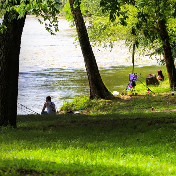 a man and a woman fishing along the Chattahoochee river surrounded by lush green grass and trees at McIntosh Reserve Park in Whitesburg Georgia