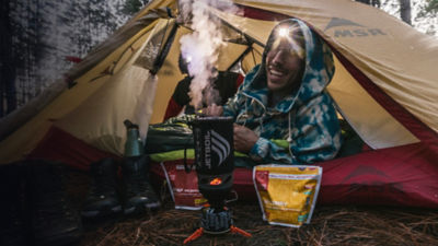 A man camping prepares a meal from his tent