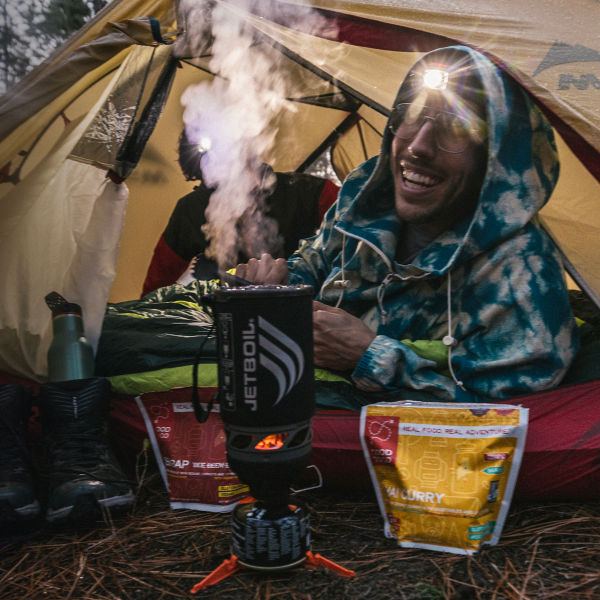 A man camping prepares a meal from his tent