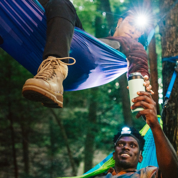 Two people lay in two hammocks and share a drink