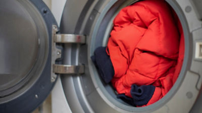 Open front door loading washing machine with dirty down jacket inside, close up, preparation for cleaning.