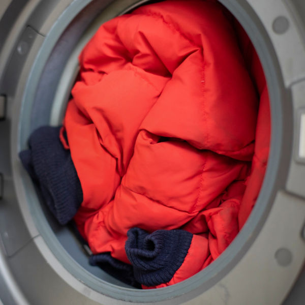 Open front door loading washing machine with dirty down jacket inside, close up, preparation for cleaning.