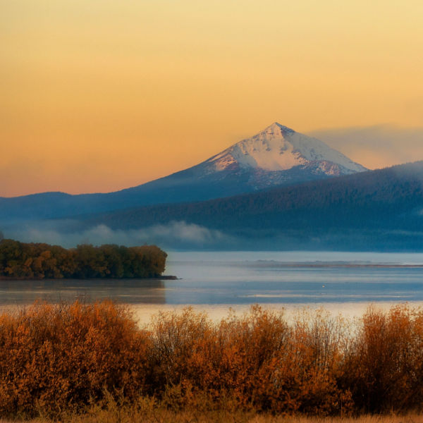 Autumn landscape of upper Klamath Lake draped in early dawn light with rising fog and Mt. McLaughlin in the backgrouns covered with a light dusting of snow.