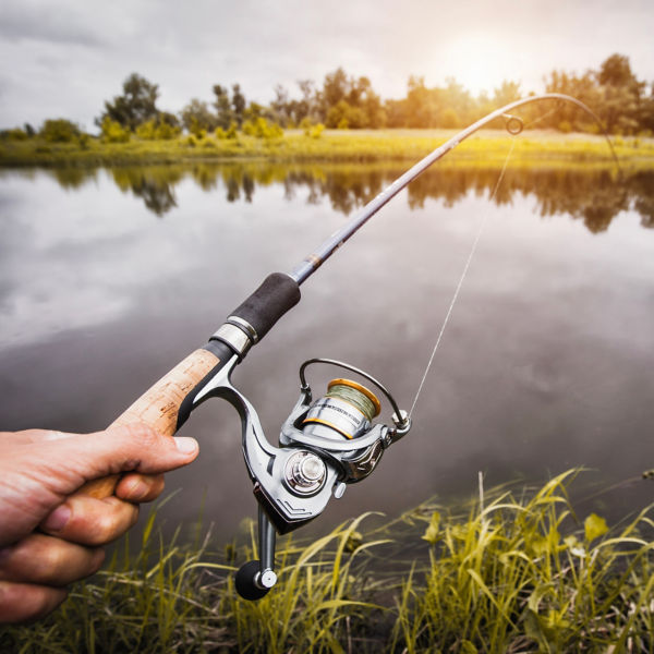 A hand with spinning and reel on the summer lake