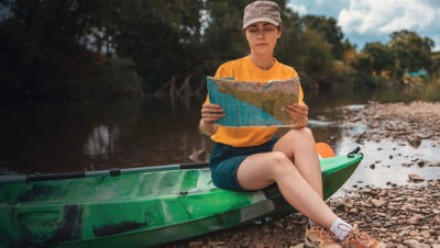 A young woman is sitting on a kayak, holding a paper map to check the route. 