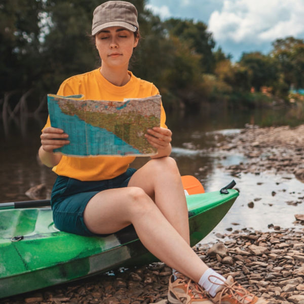 A young woman is sitting on a kayak, holding a paper map to check the route. 