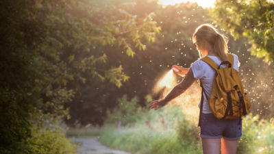 Woman is applying insect repellent against mosquito and tick on her hand during hike in nature. 