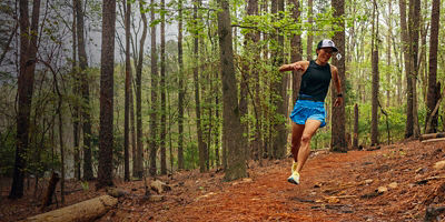 A female trail runner runs along a wooded path