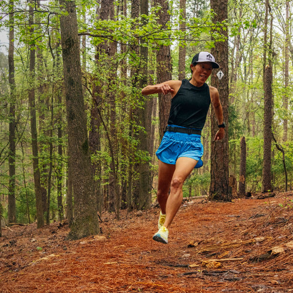 A female trail runner runs along a wooded path