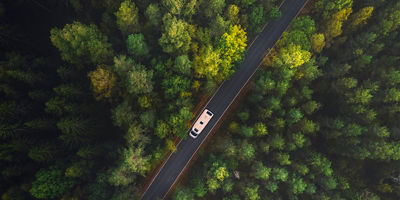 White camper van with solar panels drive through green forest