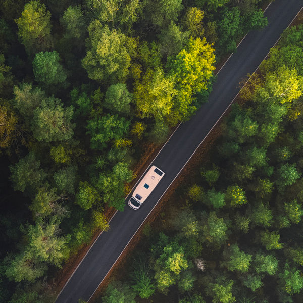 White camper van with solar panels drive through green forest