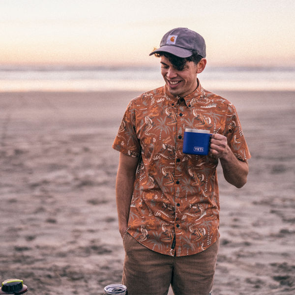 A man drinks out of a camp mug on the beach