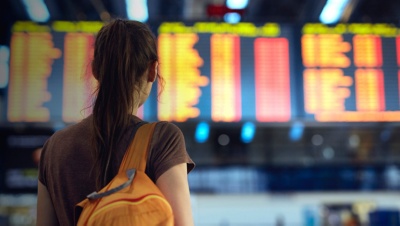 Young woman with small backpack in international airport looking at the flight information board, checking her flight