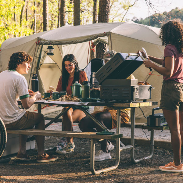Friends sit at a campsite bench while they cook