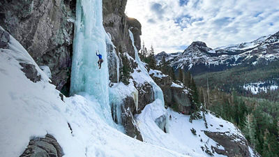 Molly Kawahata ice climbing with the mountains behind her