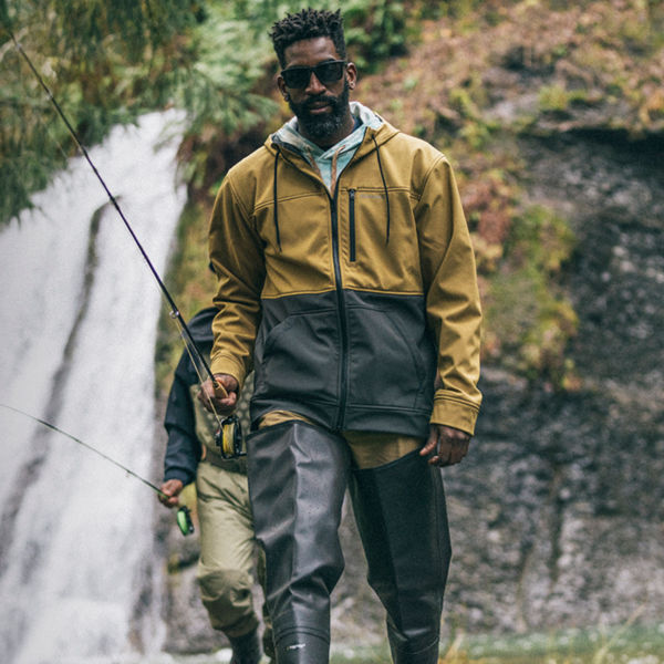 Fishermen walk with fishing poles along a river with a waterfall behind him