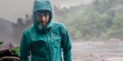 A man standing in the rain with a river and forest behind him.
