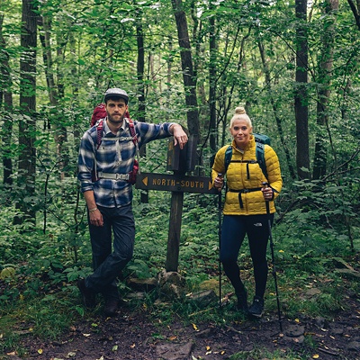 Two hikers wearing packs and using trekking poles on a trail