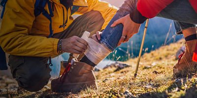 A woman has sprained her ankle while hiking, her friend uses the first aid kit to tend to the injury