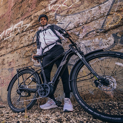 A man stands in between his bike and a stone wall.