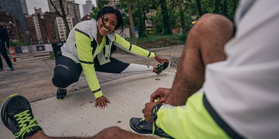 a woman stretching for a run with a man tying his shoe
