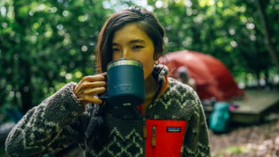 A woman drinks coffee from a camp mug