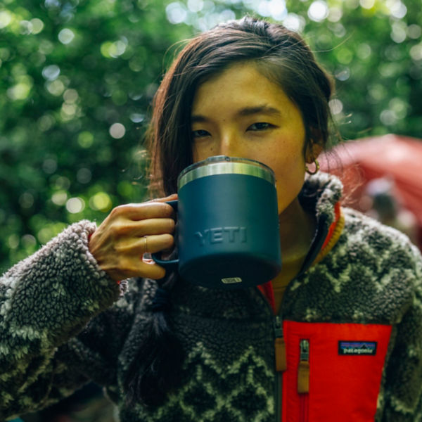 A woman drinks coffee from a camp mug