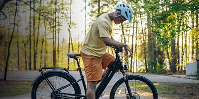 A biker wearing a helmet looks down on his bike in a forest