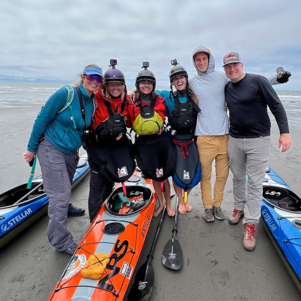The Grand Salmon team pose in front of the ocean with kayaks