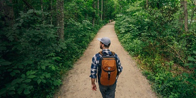 A man hikes on a lush green wooded trail