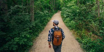 A man hikes on a lush green wooded trail