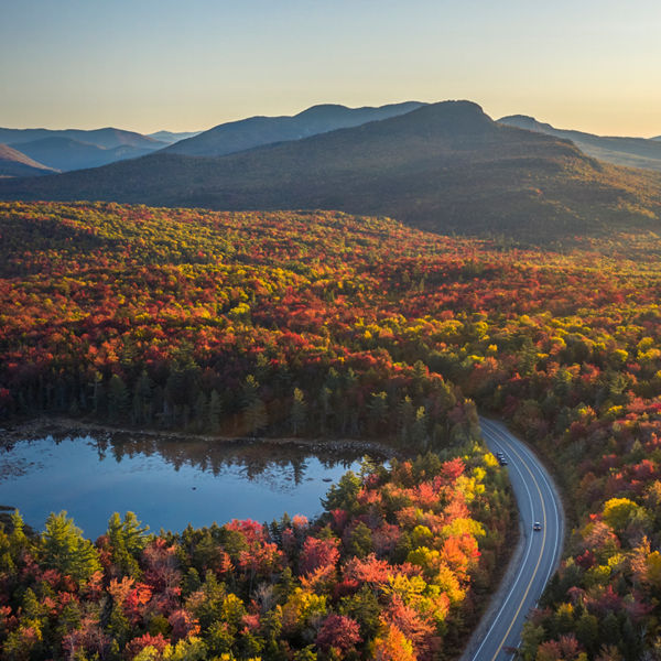 A road, highway through a forest with trees in fall colors of red, orange and yellow, lake, mountains, Kancamagus Highway, White Mountains, New Hampshier