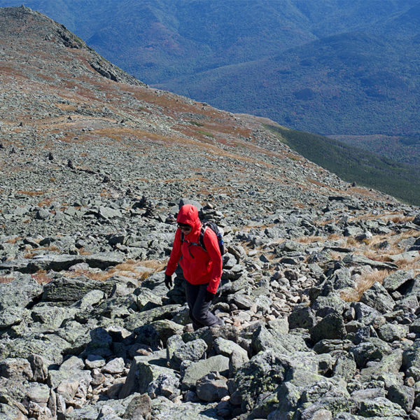 Lone hiker trekking to the summit of Mount Washington over a rocky terrain in cold windy weather
