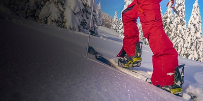 Woman splitboarding in Bohinj treks up hill covered in fresh snow.