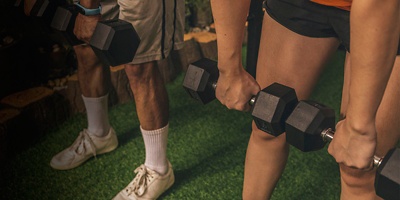 An anonymous couple does dumbbell Romanian deadlifts on the artificial grass mat of a home gym. Closeup shot.