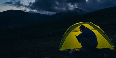 A person next to a tent at night looks on their phone