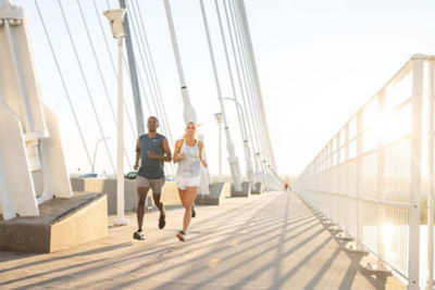 Picture of 2 runners on a bridge with low angle sunlight shining on them.
