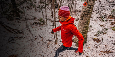 Woman in a red jacket trail running in the snow.