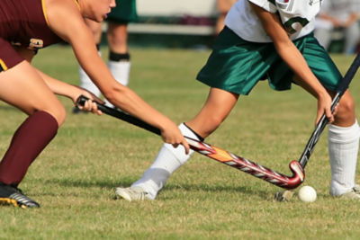 two girls in field hockey uniforms competing for a field hockey ball